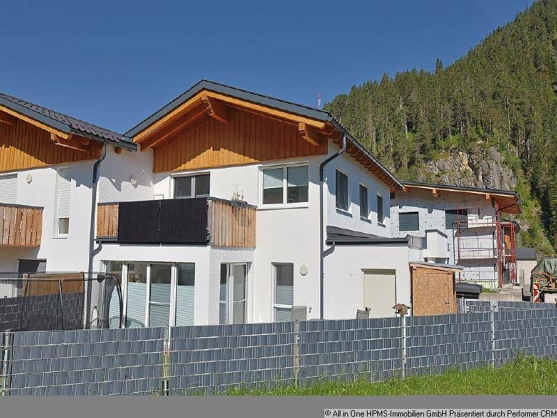 Moderne Wohnanlage mit weißer Fassade, Holzelementen und Blick auf bewaldete Berge.