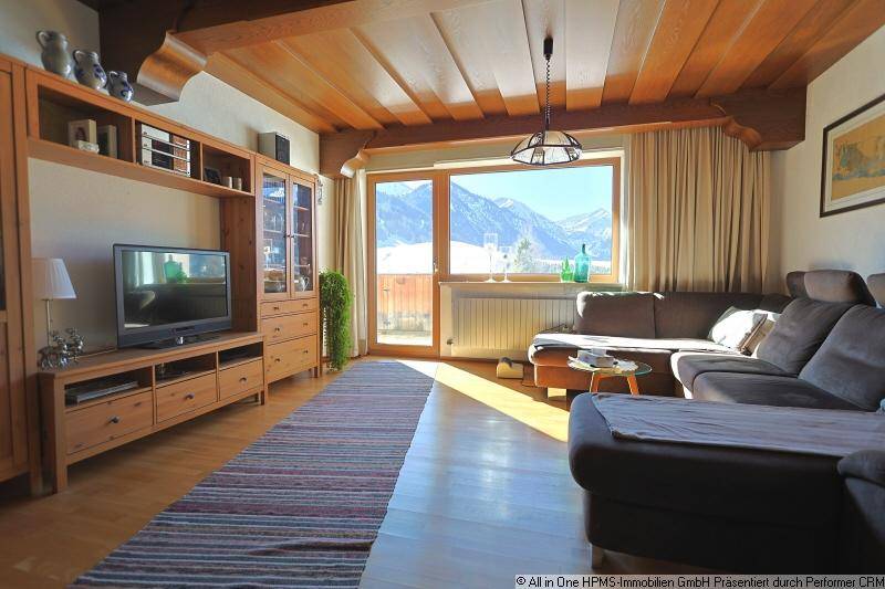 Gemütliches Wohnzimmer mit Sofa, Holzdecke und großem Fenster mit Bergblick.