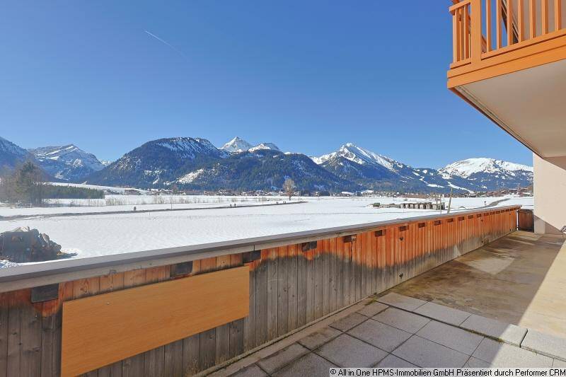 Große Terrasse mit Holzelementen und beeindruckendem Panoramablick auf die schneebedeckten Berge.