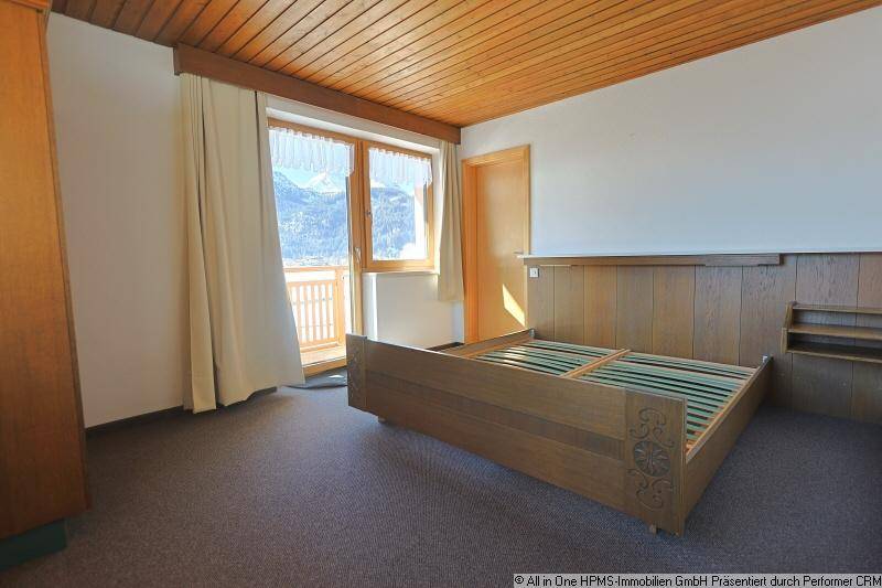 Schlafzimmer mit Holzbett, Holzdecke und Balkonzugang mit Bergblick.