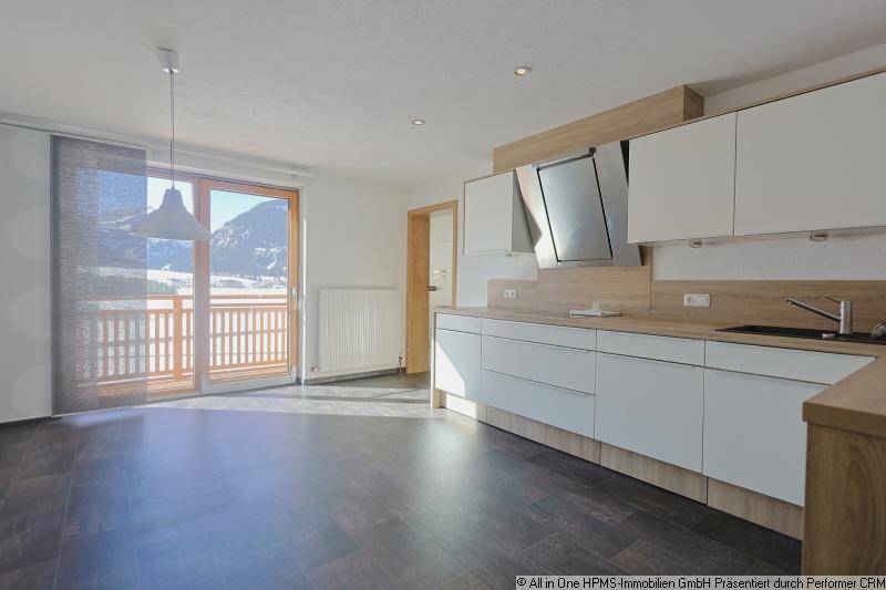 Helle, unmöblierte Küche mit Balkonzugang und Blick auf die verschneite Berglandschaft.