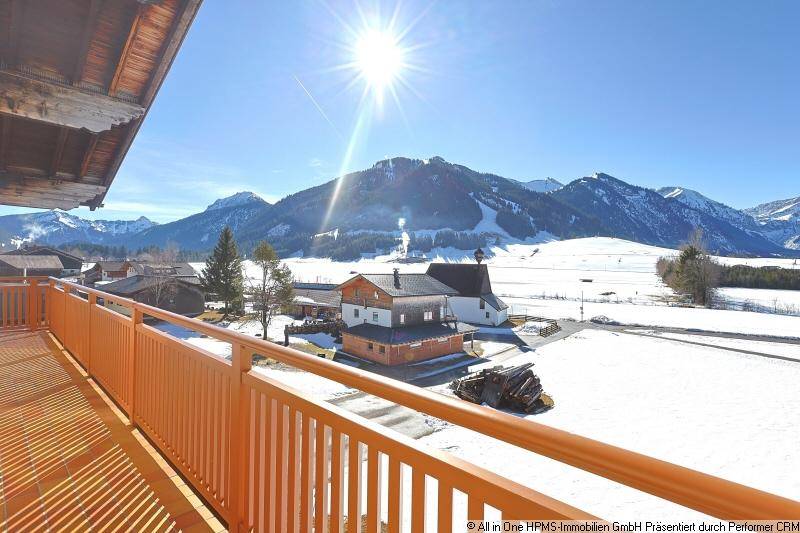 Sonniger Balkon mit Holzgeländer und weitem Blick auf die verschneite Berglandschaft.