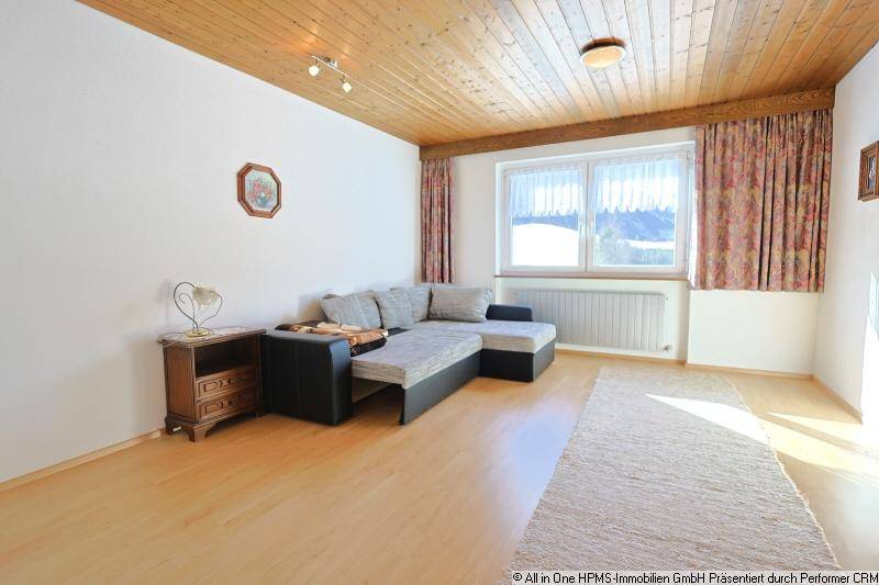 Helles Wohnzimmer mit Sofa, Holzdecke und Fenster mit Blick auf die verschneite Landschaft.