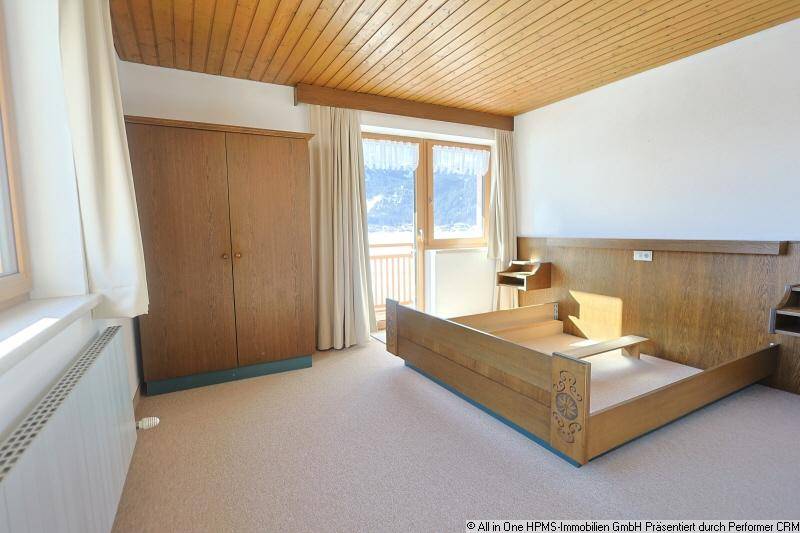 Gemütliches Schlafzimmer mit Holzbalkendecke, Teppichboden und Zugang zum Balkon mit Bergblick.