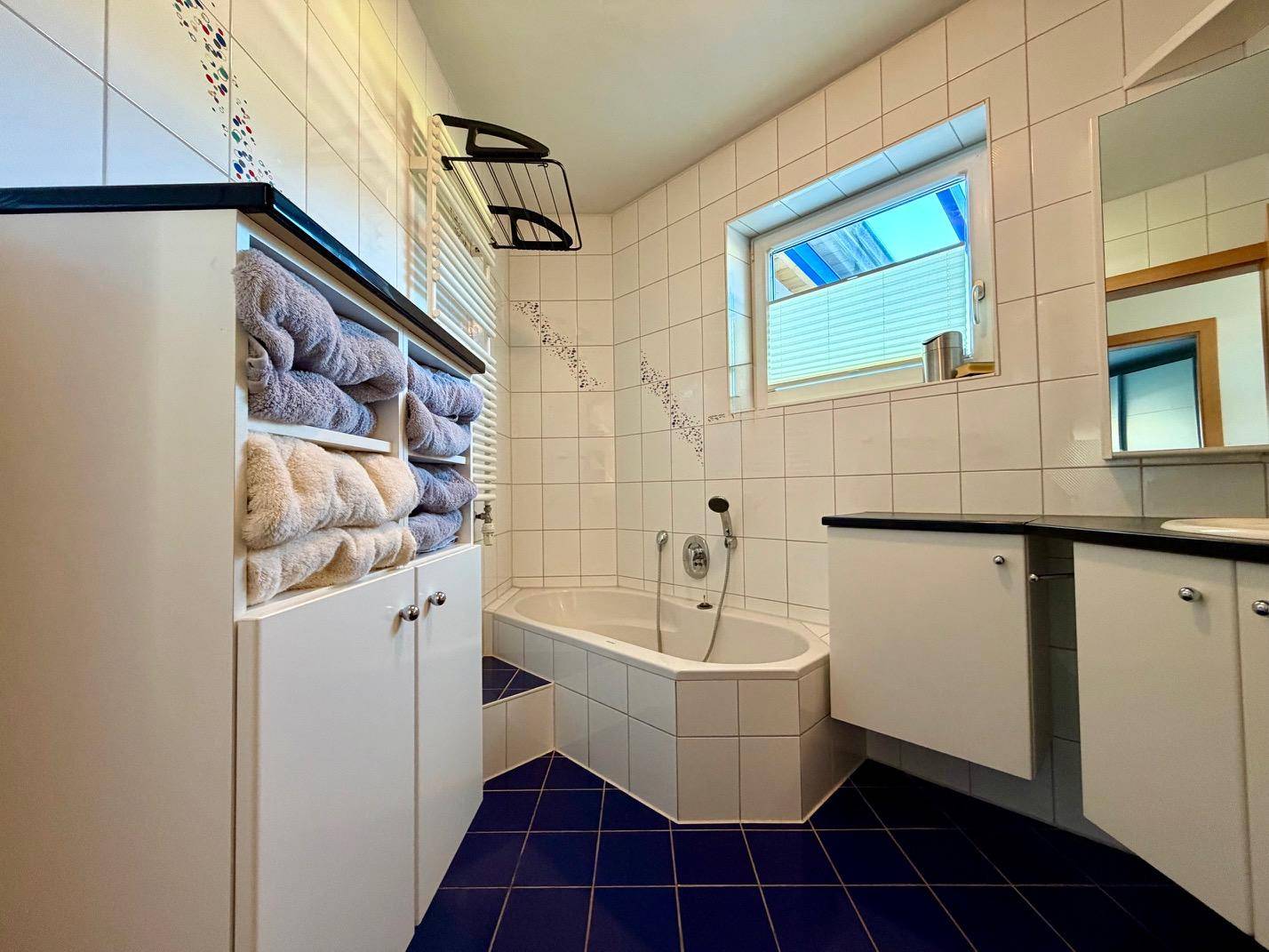 Badezimmer mit Eckbadewanne, blauen Fliesen und Fenster für Tageslicht.
