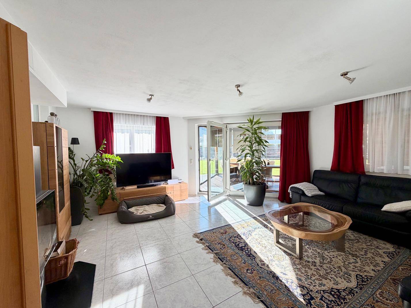 Helles Wohnzimmer mit Fliesenboden, dunklem Sofa und Zugang zur Terrasse.