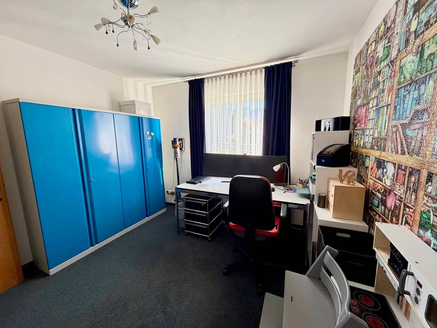 Arbeitszimmer mit blauem Schrank, Schreibtisch und Teppichboden.