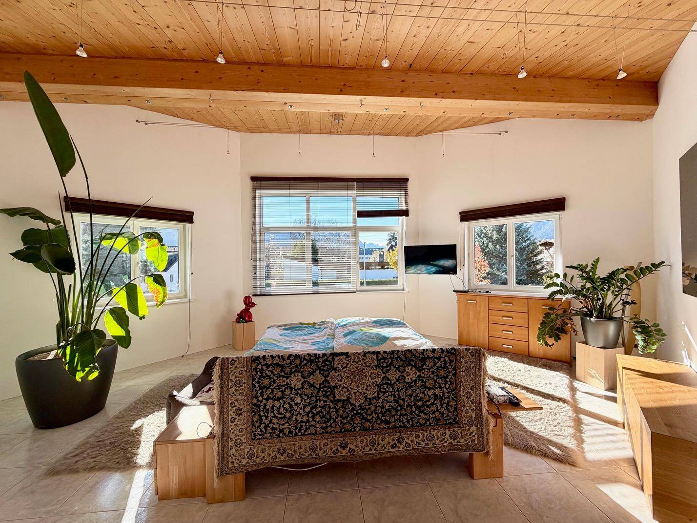 Helles Schlafzimmer mit Holzbalkendecke, Fliesenboden und Blick ins Grüne.