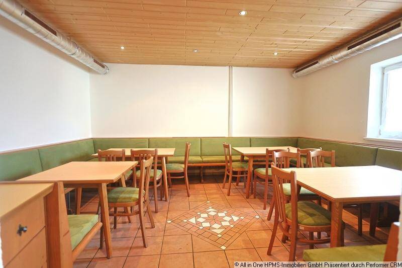 Heller Essbereich mit Holztischen, grünen Sitzbänken und einem dekorativen Fliesenmuster auf dem Boden, gut beleuchtet.