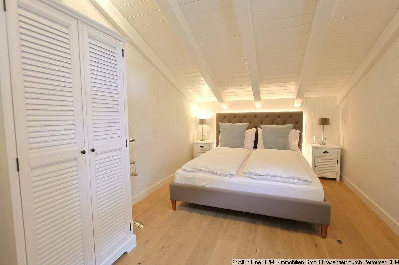 Helles Schlafzimmer im Dachgeschoss mit Holzbalkendecke, Doppelbett und weißem Kleiderschrank.