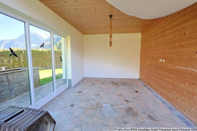 Heller Raum mit großen Schiebetüren, Holzwand und Blick auf den Garten und die Berge.