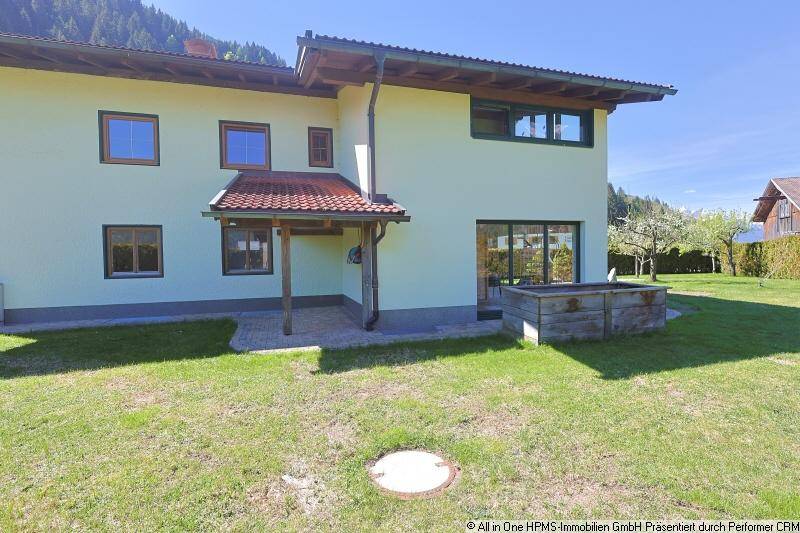 Rückseite eines Hauses mit großem Garten, Rasenfläche und Blick auf die umliegende Natur.