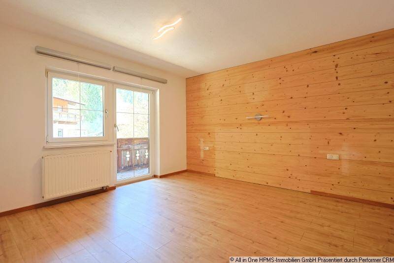 Schlafzimmer mit Holzwand, Laminatboden und Zugang zu einem kleinen Balkon.