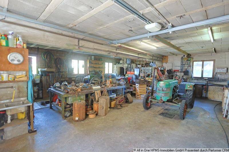 Große Garage oder Werkstatt mit einem Traktor, Werkbänken und verschiedenen Geräten.