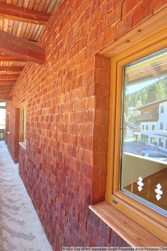 Detailansicht einer Fassade mit Holzschindeln und einem Fensterrahmen aus Holz.
