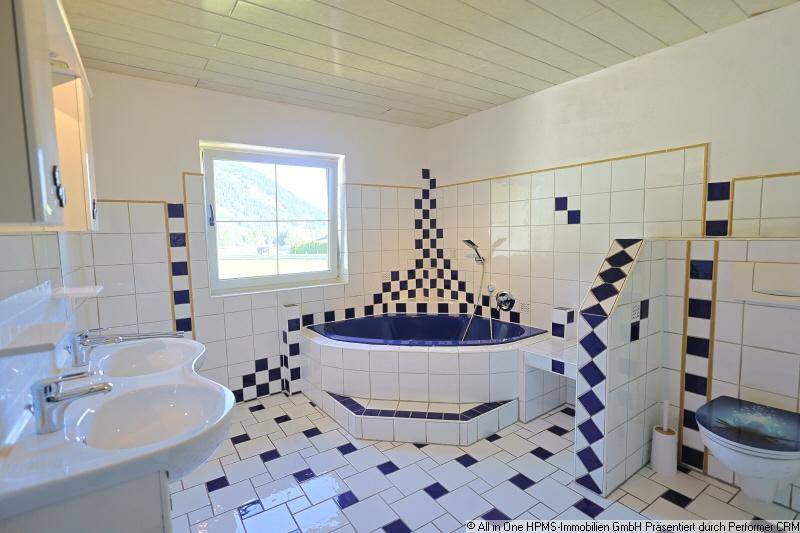 Geräumiges Badezimmer mit blauen und weißen Fliesen, Eckbadewanne und Doppelwaschbecken.