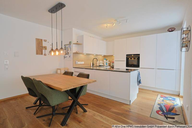 Moderne offene Küche mit Essbereich, weißen Schränken, Holzboden und Pendelleuchten.