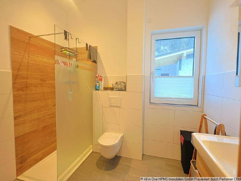 Helles Badezimmer mit begehbarer Dusche, Wand-WC, Waschbecken und Fenster für Tageslicht.