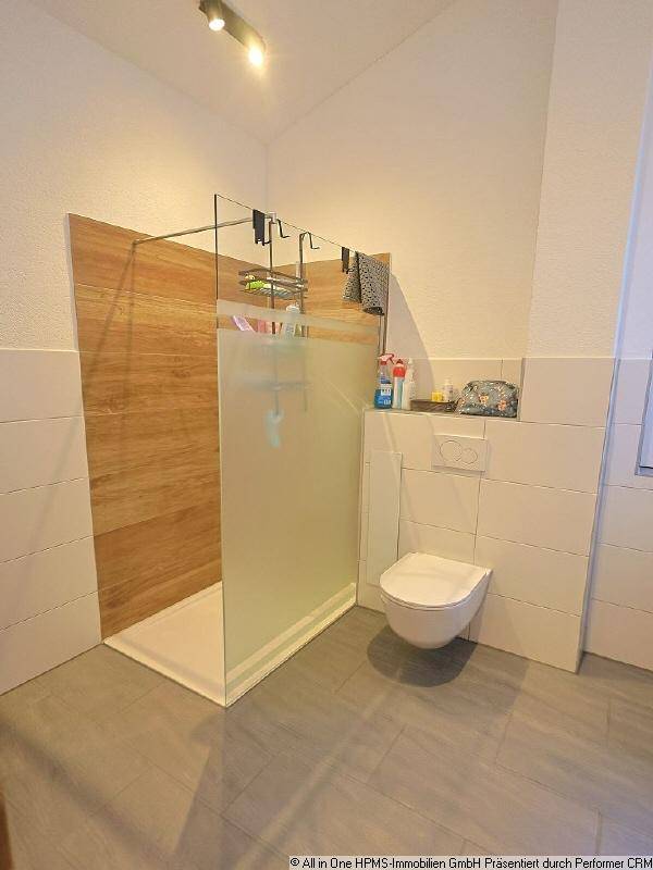 Modernes Badezimmer mit begehbarer Dusche, Wand-WC und hellen Fliesen in zeitgemäßem Design.
