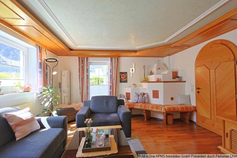 Gemütliches Wohnzimmer im alpinen Stil mit Holzbalkendecke, Kachelofen und Parkettboden.