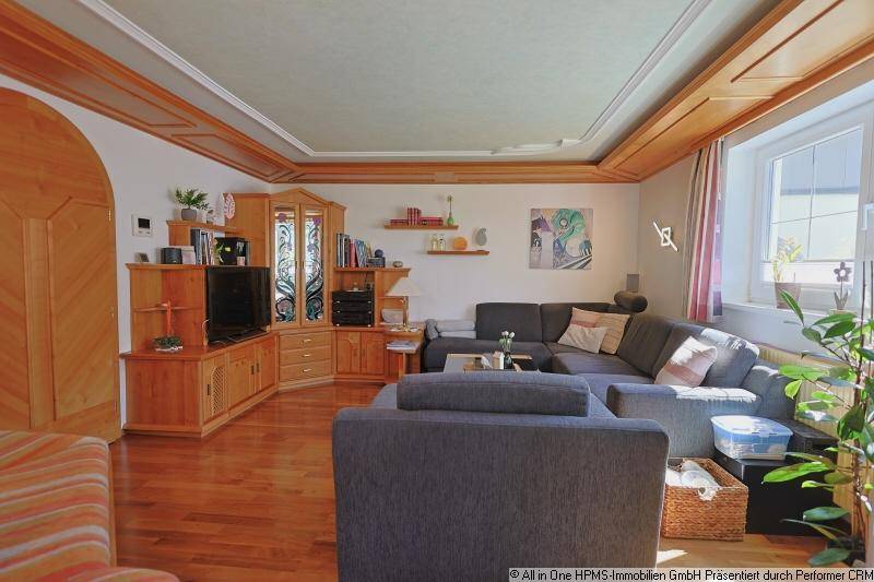 Traditionelles Wohnzimmer mit großem Ecksofa, Holzmöbeln und Blick auf den Kachelofen.