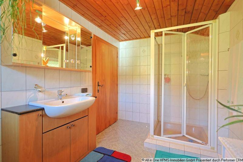 Badezimmer mit Dusche, Einzelwaschbecken und Holzdecke, hell gefliest.