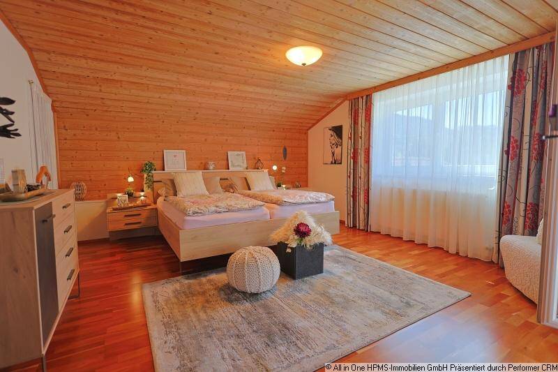 Schlafzimmer mit Holzwänden und -decke, Doppelbett und großem Fenster mit Vorhängen.