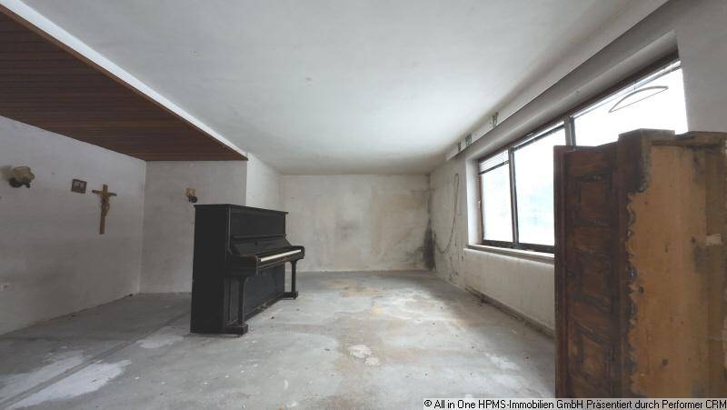 Leerer Raum mit einem Klavier, großen Fenstern und sichtbaren Gebrauchsspuren an Wänden und Boden.