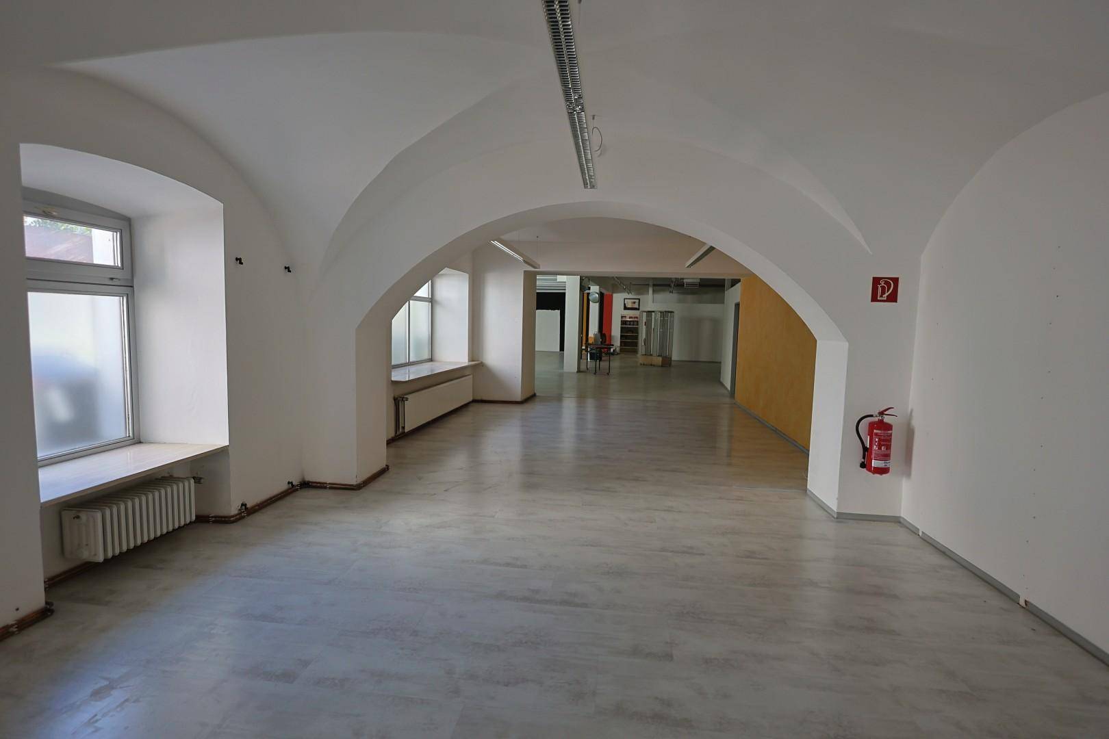Geräumiger Gewerberaum mit gewölbten Decken, großen Fenstern und einem Feuerlöscher an der Wand.