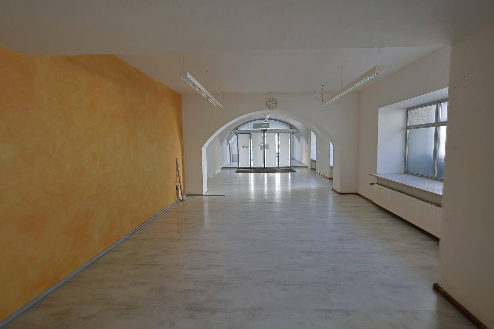 Langer Gewerberaum mit gewölbten Decken, einer gelben Akzentwand und großen Fenstern am Ende.