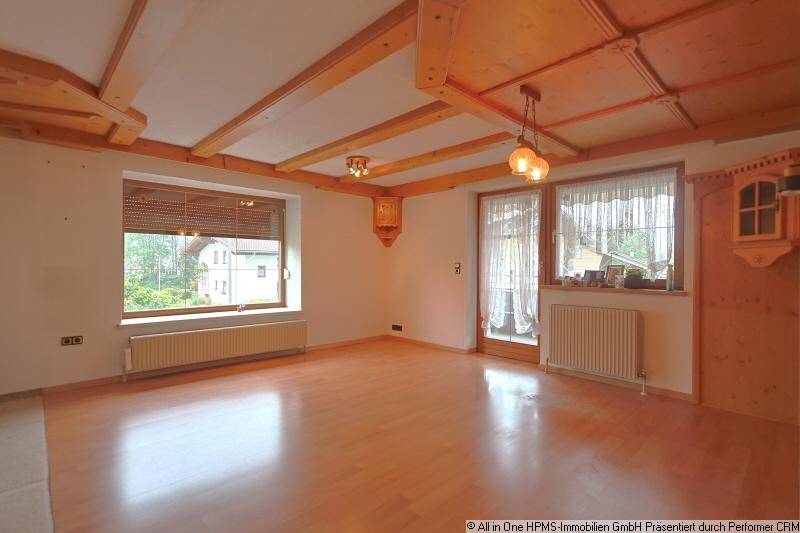 Geräumiges Wohnzimmer mit sichtbaren Holzdeckenbalken, hellem Parkettboden und großen Fenstern.