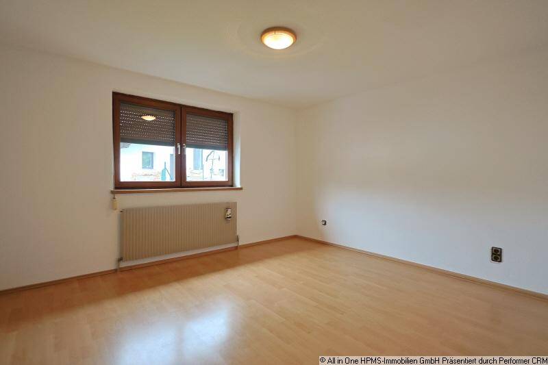 Helles Schlafzimmer mit Parkettboden, weißen Wänden und einem Fenster mit Rollladen.
