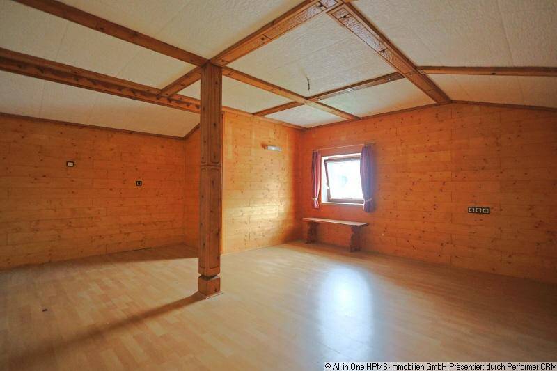 Rustikaler Raum im Dachgeschoss mit Holzverkleidung an Wänden und Decke sowie hellem Holzboden.
