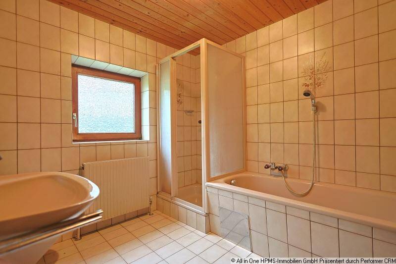 Gefliestes Badezimmer mit Badewanne, Duschkabine, Waschbecken und einem Fenster für Tageslicht.