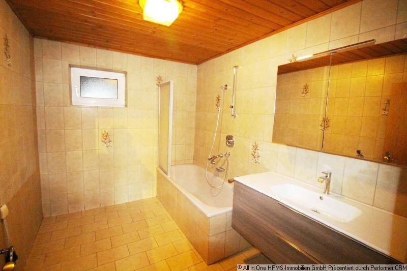 Badezimmer mit beigen Fliesen, Badewanne mit Dusche und modernem Waschtisch.