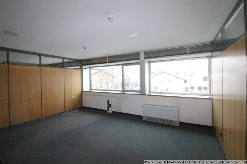 Leeres Büro mit großen Fenstern, Teppichboden und Holzvertäfelungen an den Wänden.