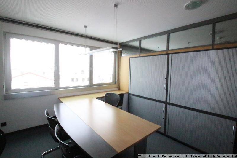 Büro mit langem Tisch, Stühlen, großen Fenstern und modernen Trennwänden mit Lamellen.