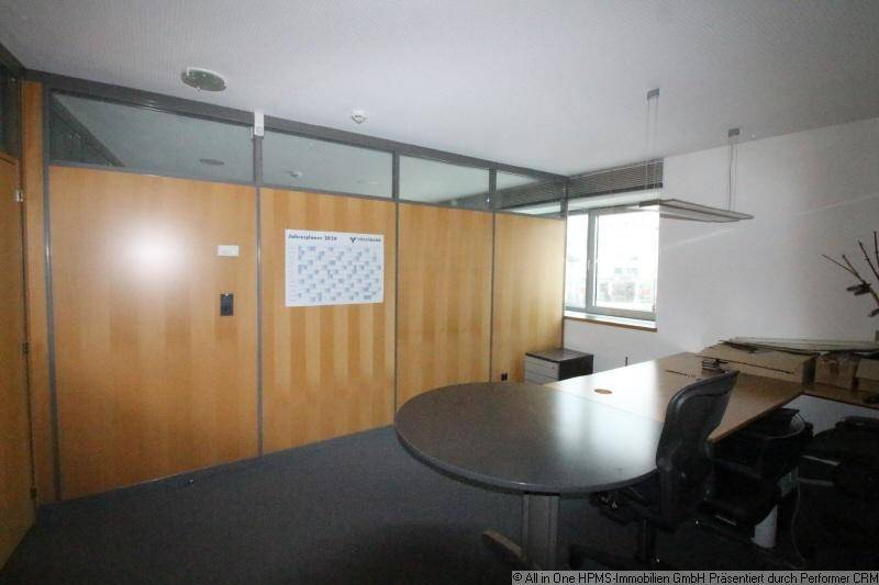 Büro mit rundem Tisch, Stühlen, Holz-Glastrennwänden und einem Fenster für Tageslicht.