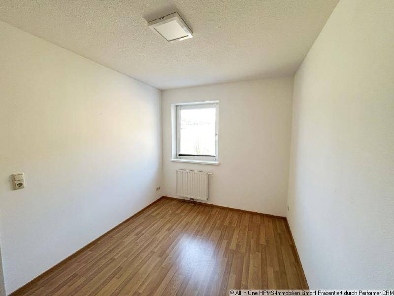 Weiteres Schlafzimmer mit hellem Parkettboden, weiß gestrichenen Wänden und einem Fenster.