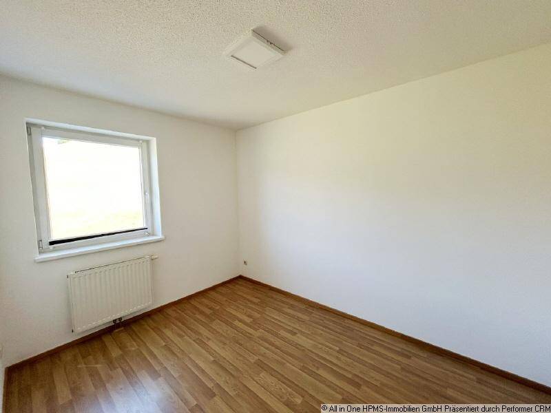 Einfaches Schlafzimmer mit Parkettboden, weiß gestrichenen Wänden und einem Fenster.