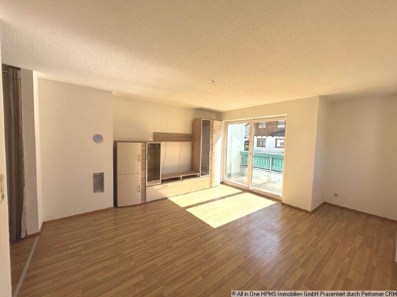 Helles Wohnzimmer mit Parkettboden, Einbauschränken und Zugang zu einem Balkon.