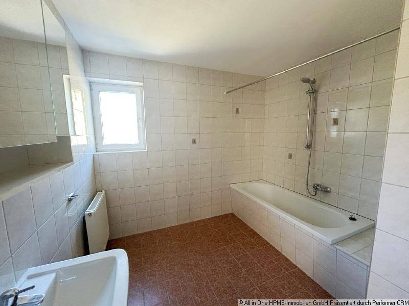Badezimmer mit Badewanne, Waschbecken, Fenster und weißen Fliesen an den Wänden.