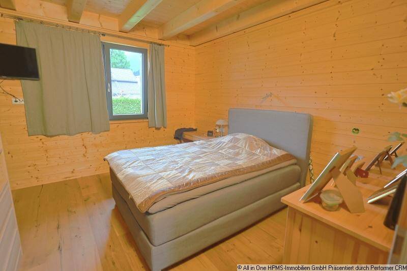 Helles Schlafzimmer mit Holzwänden, Holzbalkendecke und einem bequemen Doppelbett.