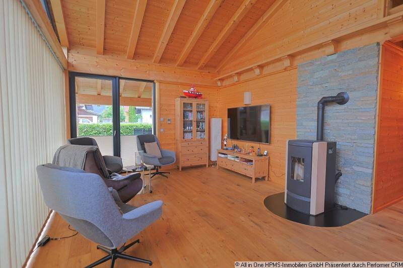 Gemütliches Wohnzimmer mit Holzwänden, Kaminofen und großen Fenstern für viel Tageslicht.