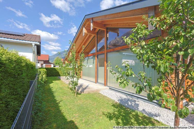 Seitlicher Blick auf das moderne Holzhaus mit großen Glasflächen und gepflegtem Gartenbereich.