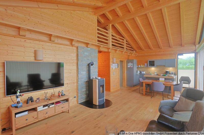Geräumiger Wohnbereich mit offener Küche, Holzbalkendecke und modernem Kaminofen als Mittelpunkt.