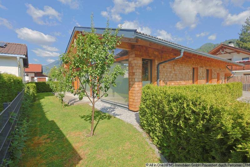 Ansicht des modernen Holzhauses von der Gartenseite mit gepflegter Hecke und Rasenfläche.