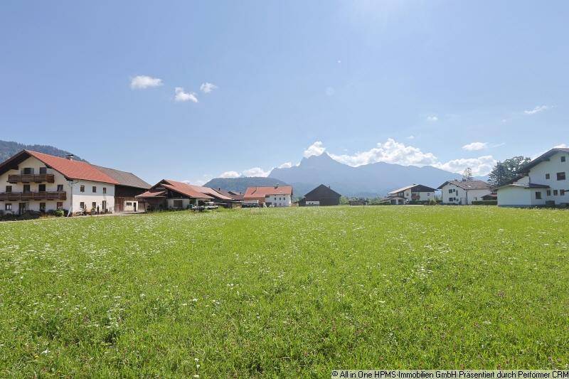 Weitläufige grüne Wiese mit traditionellen Häusern und beeindruckendem Alpenpanorama im Hintergrund.