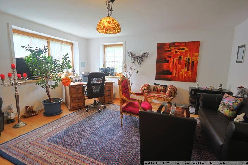 Heller Wohnbereich mit Holzschreibtisch, Zimmerpflanze und einem großen Teppich auf dem Parkettboden.