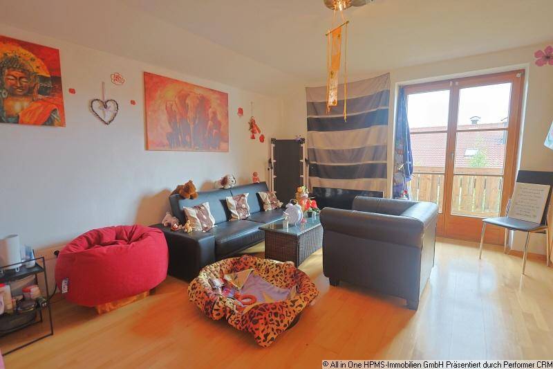Wohnbereich mit bequemer Couch, Sessel und Balkonzugang, dekoriert mit farbenfrohen Bildern und Kissen.